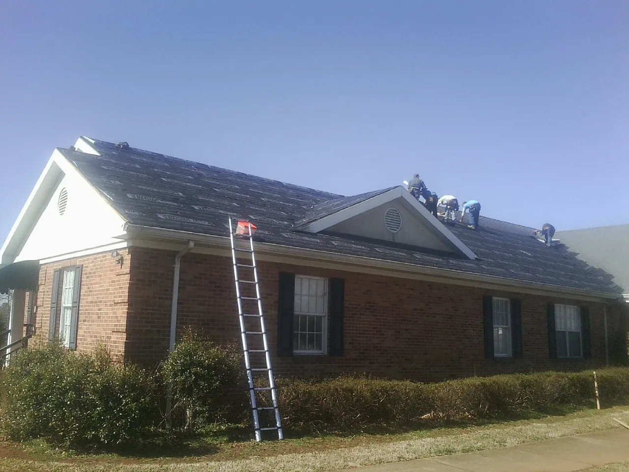 Crew tearing shingles off a brick ranch roof with a ladder set — Metal Roof Repair work by our crew in Middleport