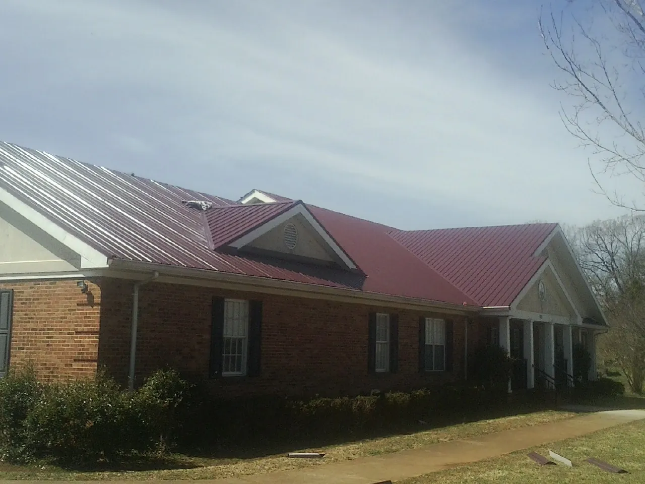 Red metal roof with gabled entries on a long brick building, from a Hail Damage Roof Repair job in Middleport