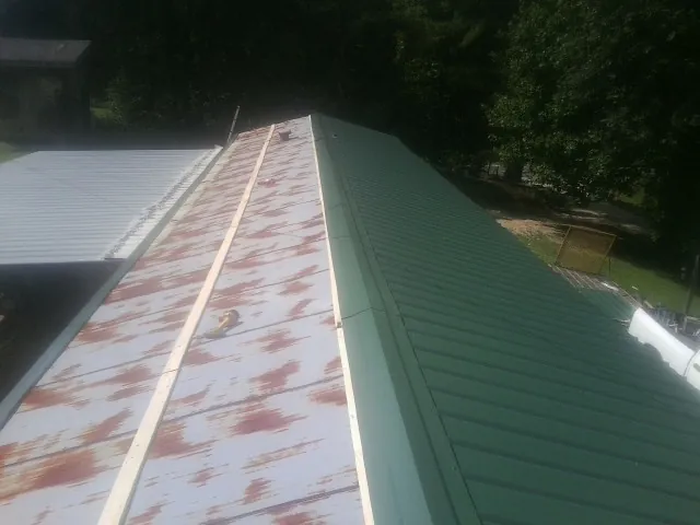Old rusted panels beside newly installed green metal roofing — Wind Damage Roof Repair by Roofing Brothers in Middleport